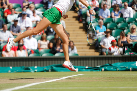 Woman mid air in tennis court with background of spectatiors hitting tennis ball