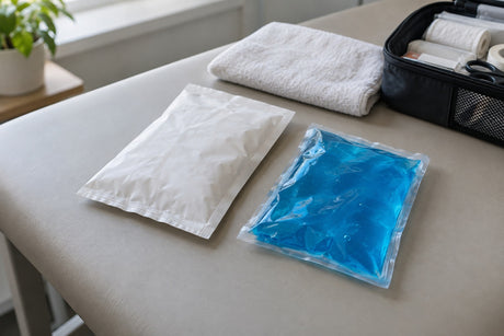 An instant white chemical ice pack and a blue reusable gel cold pack side by side on a treatment couch, with a towel and first aid bag