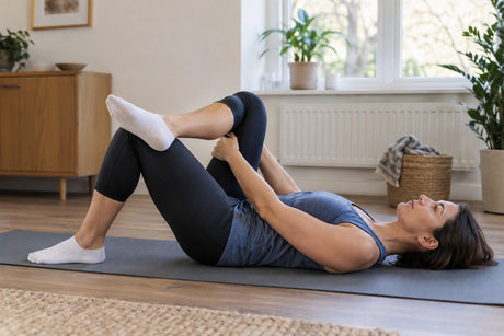 A woman lying on her back on a mat pulling one knee across her body in a piriformis stretch
