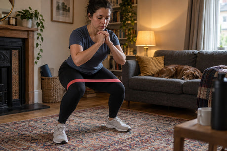 A woman doing a squat in her living room with a red resistance loop band above the knees
