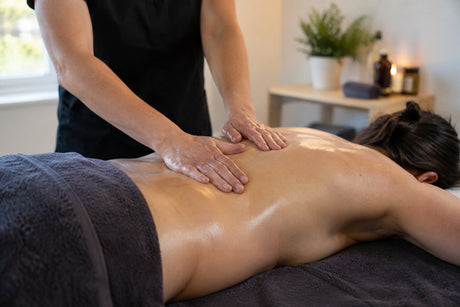 A therapist working with both hands along the oiled back of a client lying face down on a massage couch