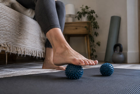 Two blue spiky massage balls on a mat with a person lowering a bare foot towards one of them