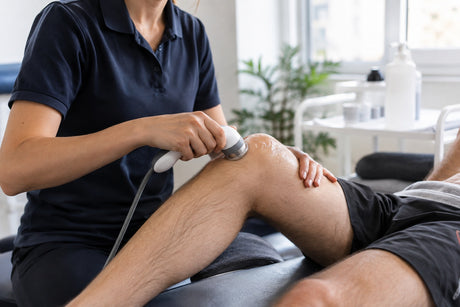 A therapist moving an ultrasound head over a patient's knee coated in gel during treatment