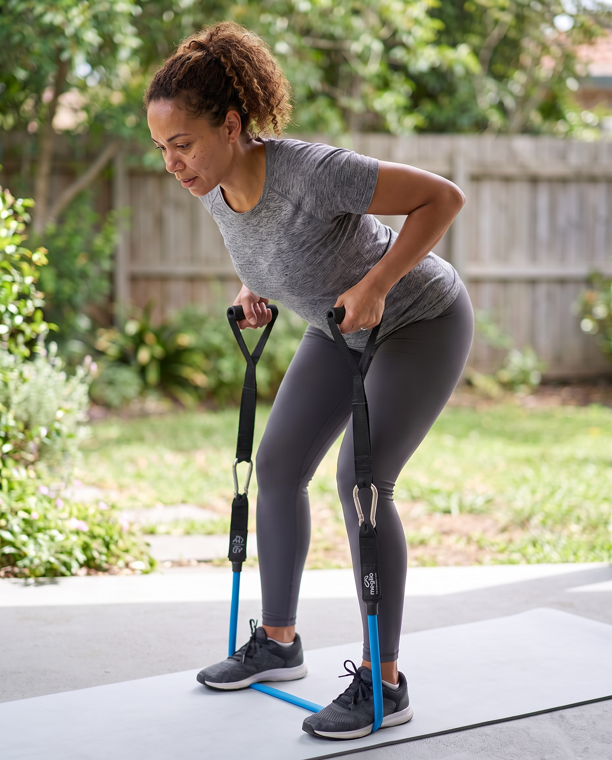 Woman performing a bent-over row with a blue resistance tube and foam handles outdoors